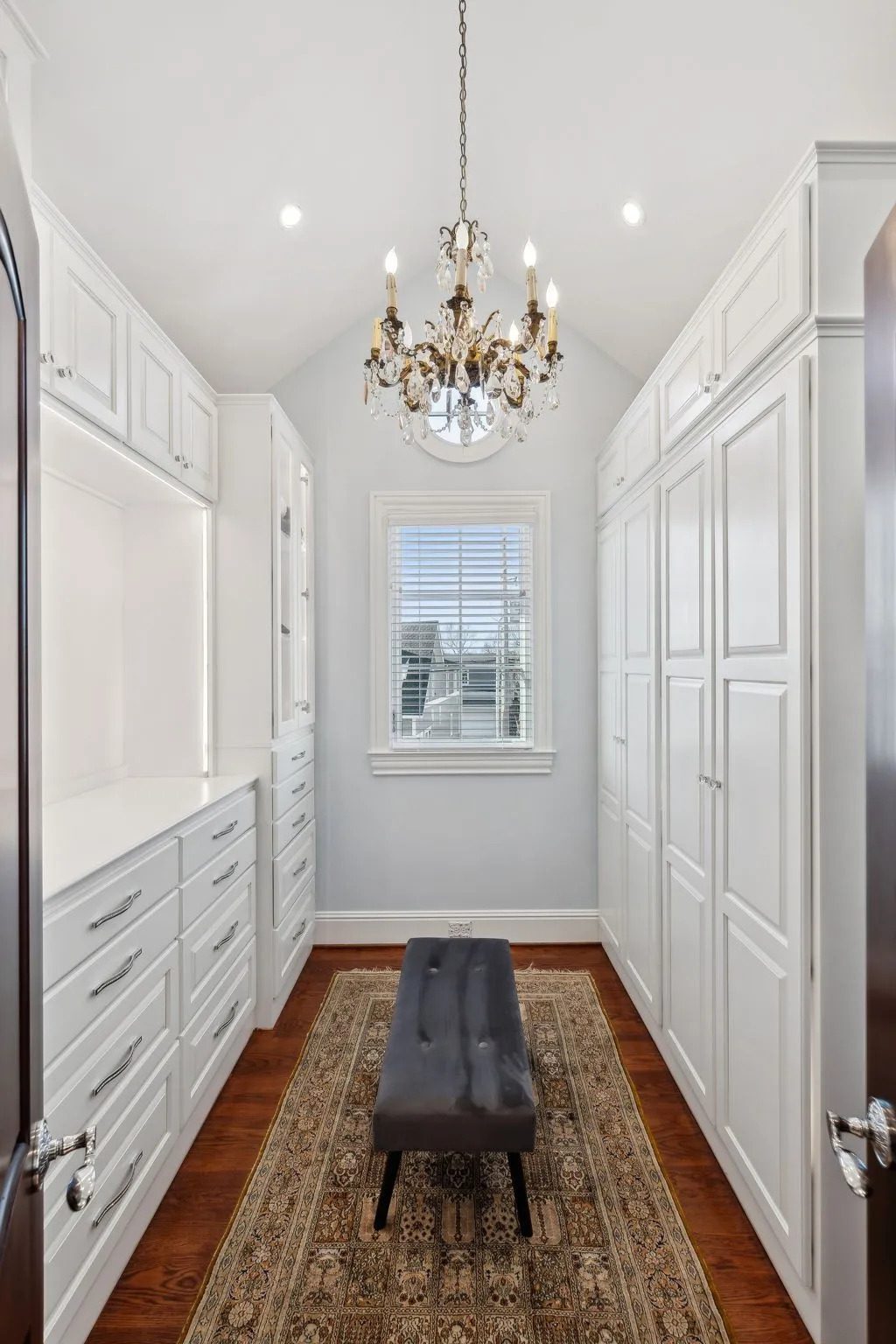 Elegant walk-in closet with white cabinetry and a crystal chandelier.