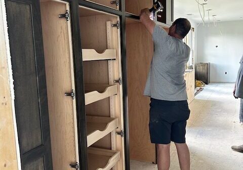 IMG_1878 A man installs wooden shelves inside a cabinet frame.